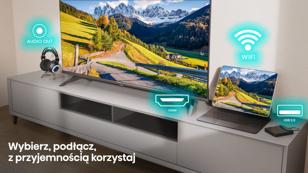 Telewizor na szafce wyświetla krajobraz górski, obok laptop z tym samym obrazem. Na ekranie widoczne są ikony: AUDIO OUT, HDMI, WIFI, USB 2.0 oraz tekst \'Wybierz, podłącz, z przyjemnością korzystaj\'.