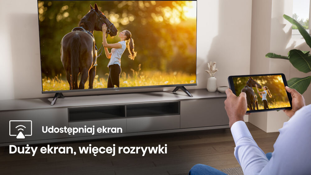 Na obrazie widać telewizor wyświetlający scenę z osobą i koniem na tle zachodzącego słońca. Na ekranie tabletu widoczny jest ten sam obraz, a na dole znajduje się tekst: \'Udostępniaj ekran Duży ekran, więcej rozrywki\'.