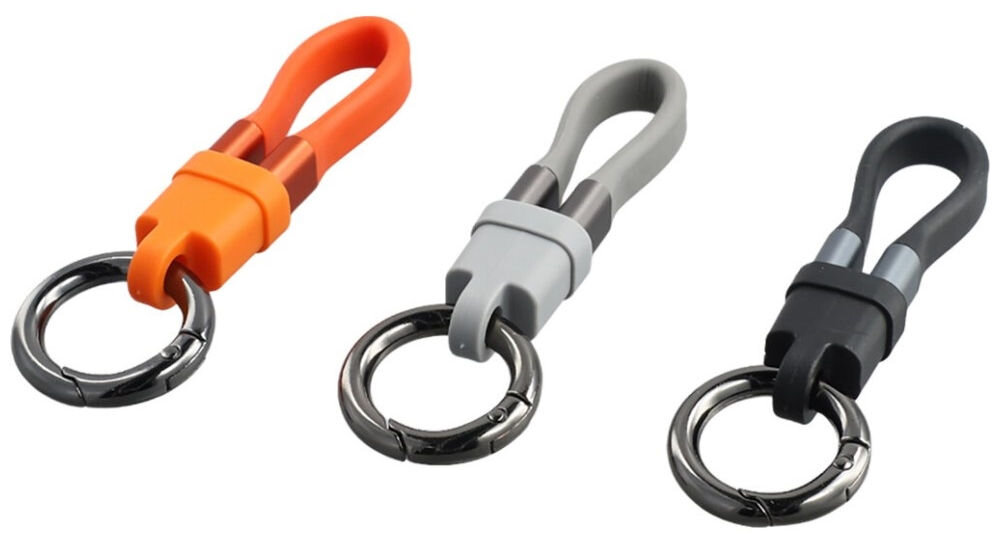 Na obrazie widoczne są trzy breloki z kablami USB-C w kolorach pomarańczowym, szarym i czarnym. Każdy brelok ma metalowy pierścień do przypięcia kluczy.