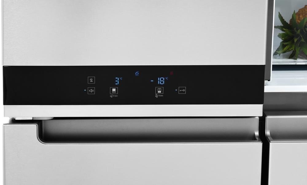 Panel sterowania lodówki z wyświetlaczem cyfrowym pokazującym temperatury 3°C i -18°C oraz ikonami funkcji. Obok panelu widoczna jest część drzwi lodówki w srebrnym kolorze.