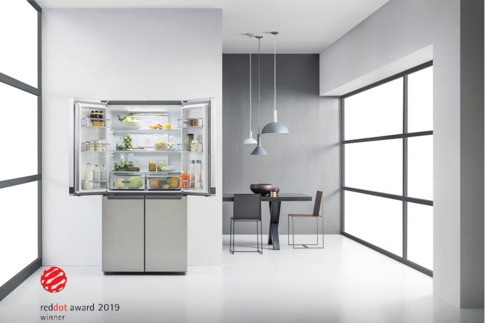 Srebrna lodówka side by side z otwartymi drzwiami, wypełniona różnymi produktami spożywczymi. W lewym dolnym rogu widoczne jest logo \'reddot award 2019 winner\'.