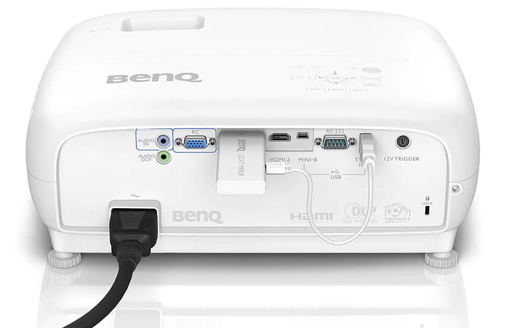 Tył białego projektora z widocznymi portami: AUDIO IN, AUDIO OUT, PC, HDMI 2, MINI-B, USB, RS-232, 12V TRIGGER. Na obudowie widoczne logo \'BenQ\'.