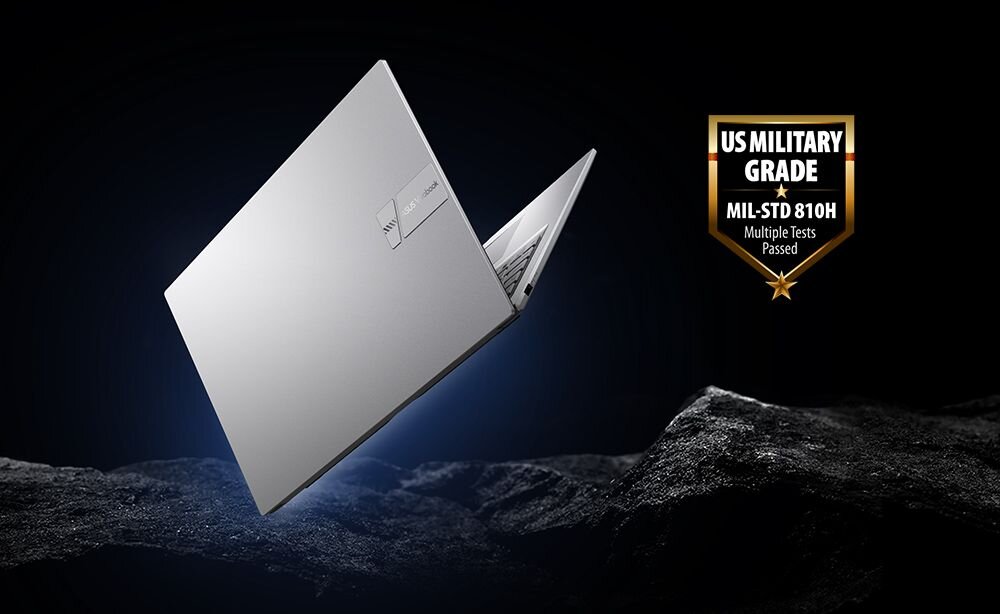 Obraz przedstawia srebrny laptop na tle ciemnego, skalistego krajobrazu. Obok laptopa widnieje odznaka z napisem \'US MILITARY GRADE MIL-STD 810H Multiple Tests Passed\'.