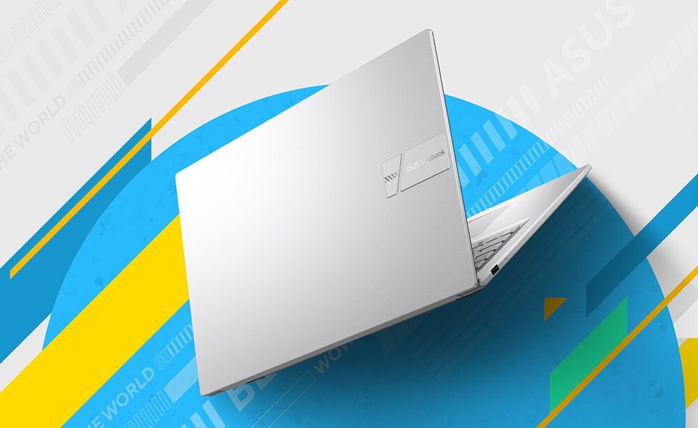 Srebrny laptop z widocznym logo \'ASUS\' na pokrywie, umieszczony na tle z kolorowymi wzorami i napisami. Na obrazie widoczny jest również tekst \'VIVBOOK\'.