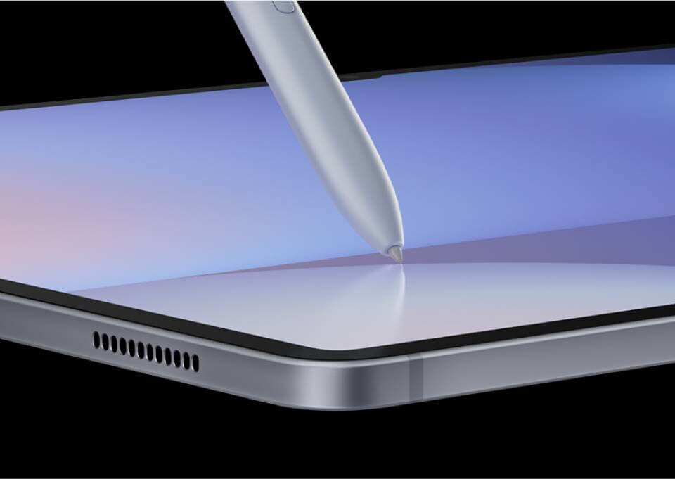 Obraz przedstawia srebrny tablet z dużym ekranem, na którym znajduje się rysik dotykający powierzchni. Widać również otwory głośnika na krawędzi urządzenia.