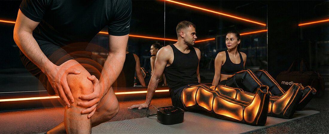 Osoba siedzi na macie w pomieszczeniu z lustrami, używając masażera limfatycznego do nóg, który emituje pomarańczowe światło. Obok znajduje się urządzenie sterujące, a w tle widoczne jest logo \'medivon\'.
