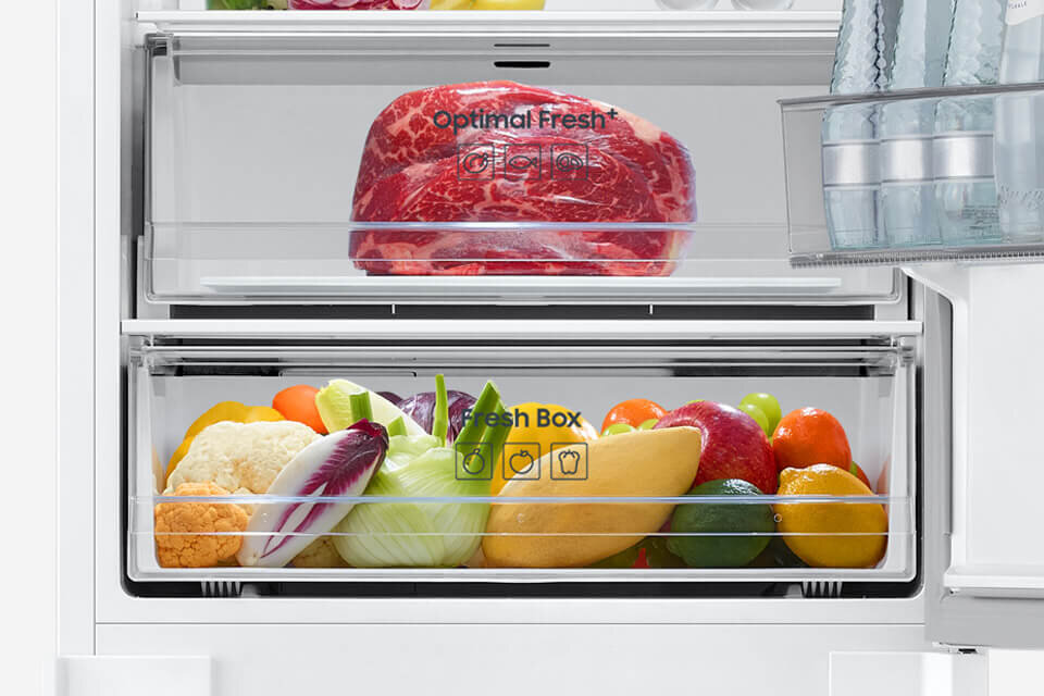 Wnętrze lodówki z dwiema szufladami, w górnej znajduje się kawałek mięsa z napisem \'Optimal Fresh\', a w dolnej różnorodne warzywa i owoce z napisem \'Fresh Box\'.
