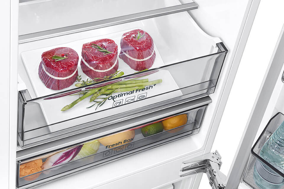 Wnętrze lodówki z widocznymi dwoma szufladami. Na górnej szufladzie napis \'Optimal Fresh+\', a w środku znajdują się kawałki mięsa i szparagi; dolna szuflada zawiera owoce i warzywa z napisem \'Fresh Box\'.