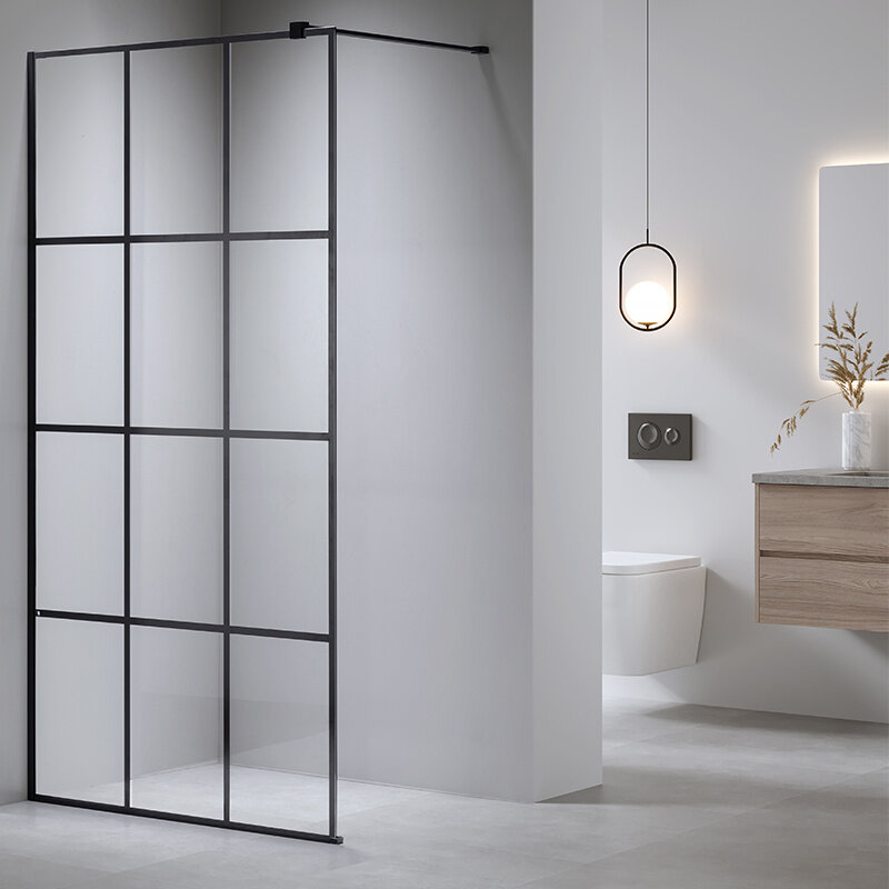 Na obrazie widoczna jest ścianka prysznicowa typu walk-in z czarną matową ramą, zamontowana w nowoczesnej łazience. W tle znajduje się wisząca lampa, toaleta podwieszana oraz szafka z umywalką.