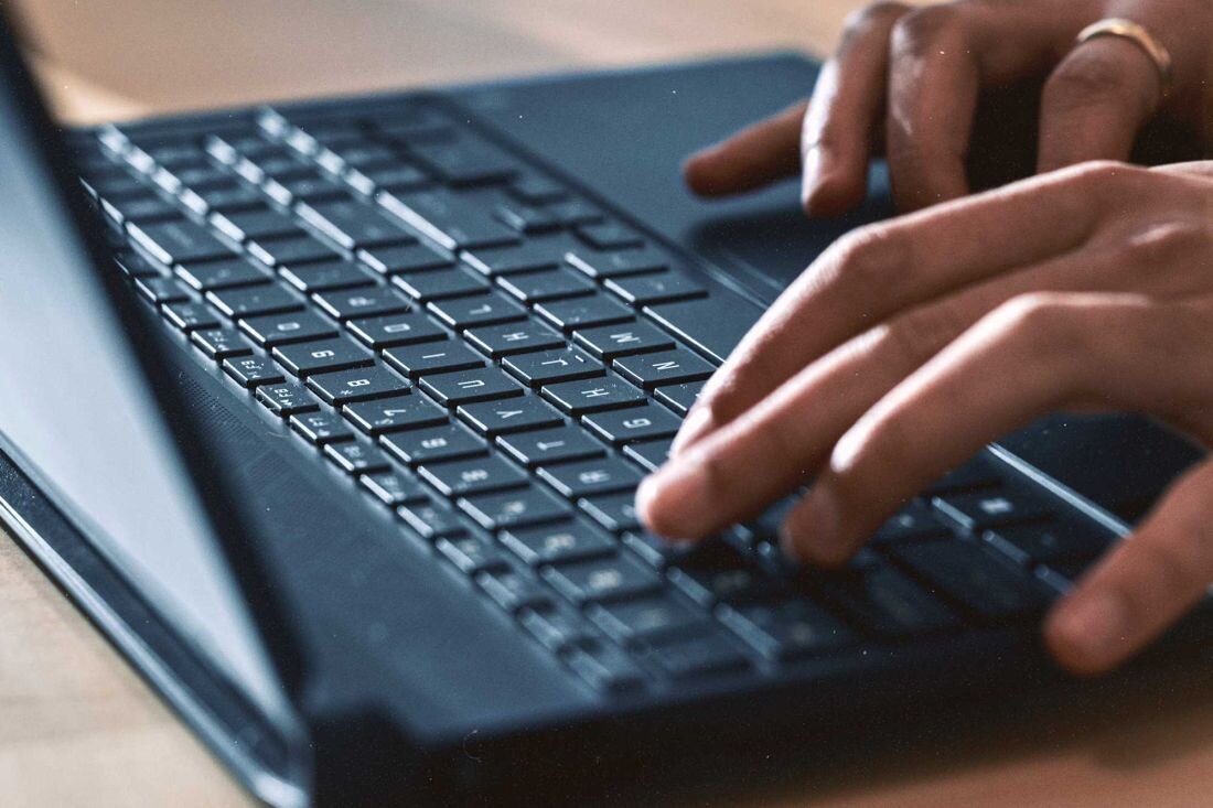 Osoba pisze na klawiaturze laptopa, widoczne są dłonie i część klawiatury.