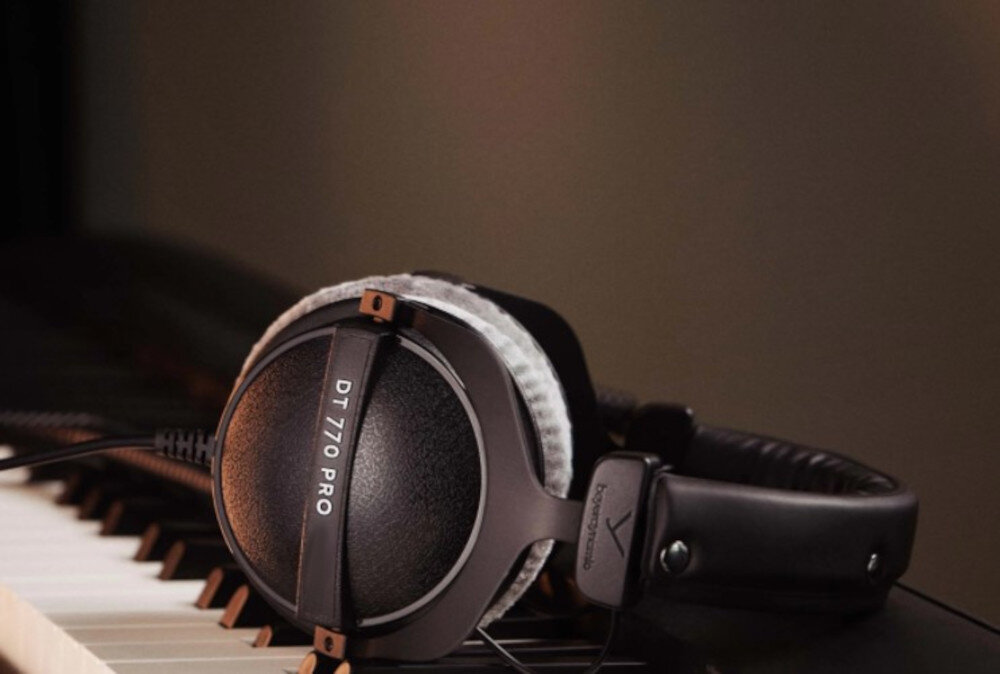 Czarne słuchawki nauszne z napisem \'DT 770 PRO\' leżą na klawiaturze pianina. Na pałąku widoczne jest logo \'beyerdynamic\'.