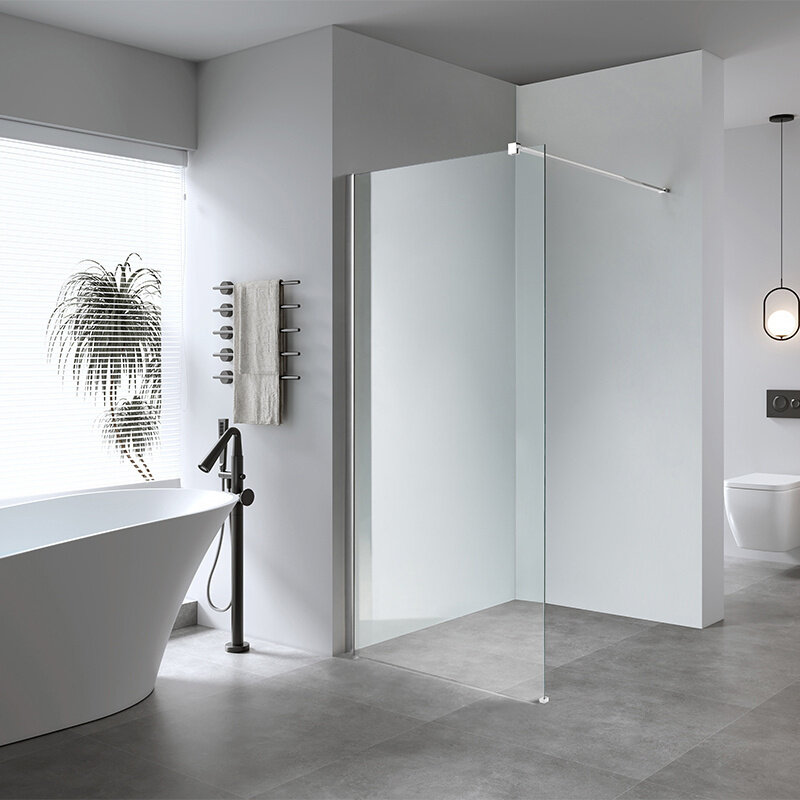 Nowoczesna łazienka z wolnostojącą wanną, szklaną ścianką prysznicową typu walk-in i minimalistycznym wystrojem. Na ścianie wisi ręcznik na chromowanym wieszaku, a przez okno wpada naturalne światło.