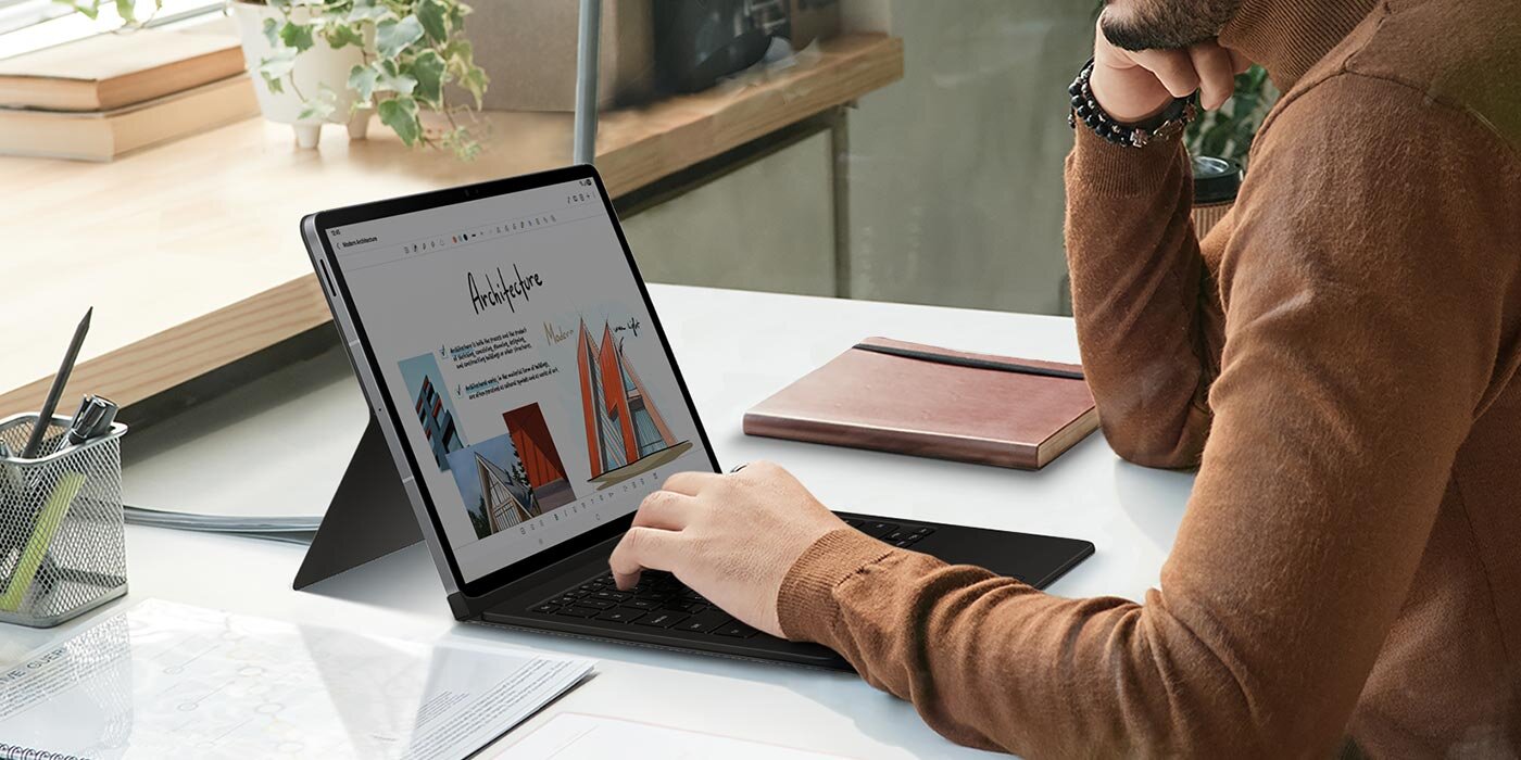 Mężczyzna korzysta z Galaxy Tab S10 FE Plus, trzymając dłoń na etui Book Cover Keyboard. Osoba siedzi przy biurku, używając tabletu z klawiaturą w czarnym etui. Na ekranie widoczny jest dokument z grafiką i tekstem dotyczącym architektury.