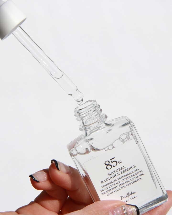 Przezroczysta butelka z pipetą zawiera esencję rozświetlającą do twarzy. Na etykiecie widnieje napis: \'85% NATURAL RADIANCE ESSENCE\'.