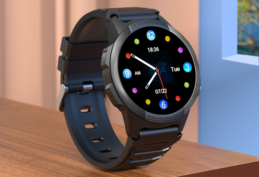 Smartwatch z okrągłym wyświetlaczem pokazuje godzinę 18:36, dzień tygodnia \'Tue\' oraz datę \'07/22\'. Tarcza zegarka ma kolorowe oznaczenia godzinowe i czarny pasek.