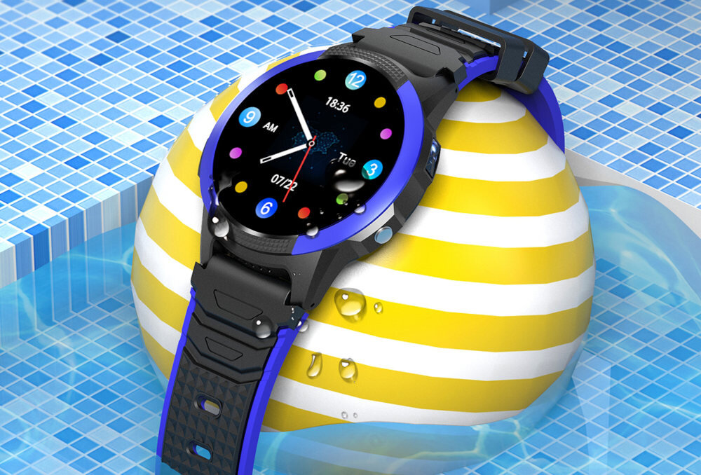 Smartwatch z niebieską obudową i czarnym paskiem leży na żółto-białej piłce w basenie. Na wyświetlaczu widoczna jest godzina 18:36, data \'Tue\', oraz kolorowe ikony aplikacji.
