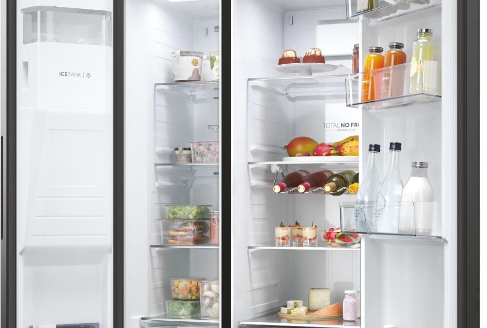 Wnętrze lodówki z widocznymi półkami wypełnionymi różnymi produktami spożywczymi, takimi jak owoce, napoje i pojemniki z jedzeniem. Na drzwiach lodówki widoczny jest napis \'ICE TANK\' oraz \'TOTAL NO FROST\'.