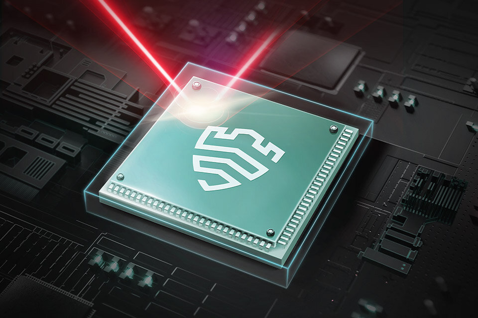 Obraz przedstawia zielony chip komputerowy z białym symbolem na powierzchni, oświetlony czerwonymi promieniami laserowymi. Chip znajduje się na tle płyty głównej z widocznymi ścieżkami i elementami elektronicznymi.