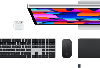 Na obrazie widoczny jest laptop z kolorowym ekranem, klawiatura, mysz oraz słuchawki bezprzewodowe. Logo producenta to nadgryzione jabłko.