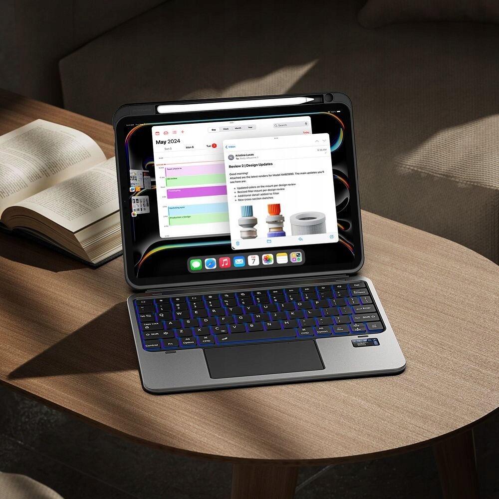 Na drewnianym stole znajduje się tablet z klawiaturą w etui, na ekranie widoczny jest kalendarz z datą maj 2024 oraz notatka z kolorowymi grafikami. Obok leży otwarta książka.
