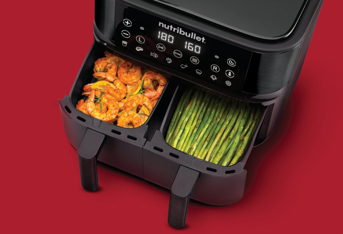 Frytkownica beztłuszczowa Nutribullet z dwoma otwartymi koszami, w jednym znajdują się krewetki, a w drugim zielone warzywa. Na panelu widoczny jest napis \'nutribullet\' oraz cyfry \'180\' i \'160\'.