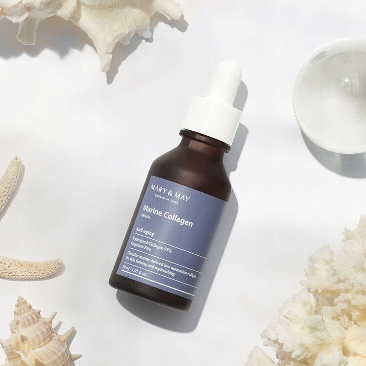 Butelka z ciemnego szkła z białą pipetą, na etykiecie napis \'MARY & MAY Marine Collagen Serum\'. W tle widoczne są muszle i koralowce.