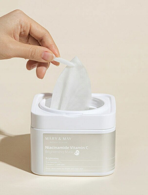 Osoba wyciąga maskę z białego pojemnika z napisem \'MARY & MAY Niacinamide Vitamin C Brightening Mask\'.