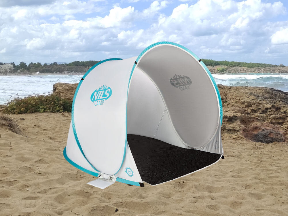 Namiot w kolorze szaro-turkusowym z logo \'NILS CAMP\' stoi na piaszczystej plaży. W tle widać morze i niebo z chmurami.