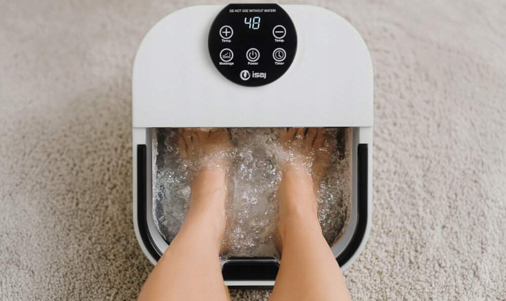 Masażer do stóp z widocznymi stopami zanurzonymi w wodzie, na panelu wyświetlacz z cyfrą 48 i przyciskami oznaczonymi jako Massage, Power, Timer oraz logo isaj.