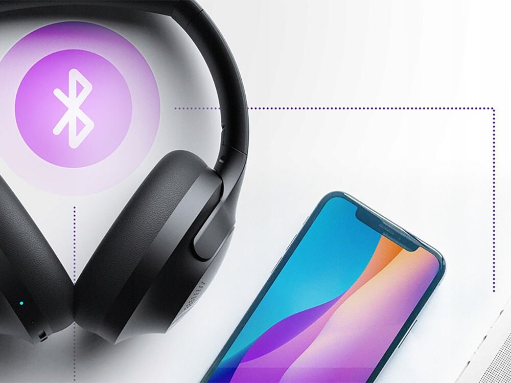 Na obrazie widoczne są czarne słuchawki nauszne oraz smartfon z kolorowym ekranem. Obok znajduje się symbol Bluetooth na fioletowym tle.