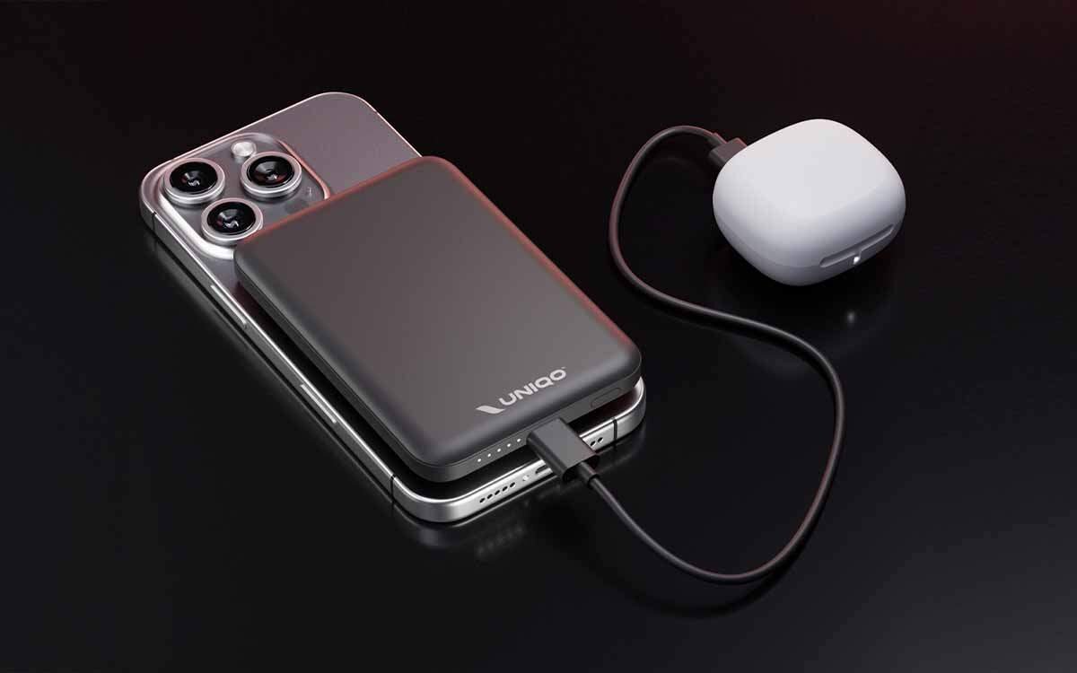 Na obrazie widoczny jest czarny powerbank z logo \'UNIQO\', podłączony do smartfona. Obok znajduje się biały, okrągły przedmiot z podłączonym kablem.