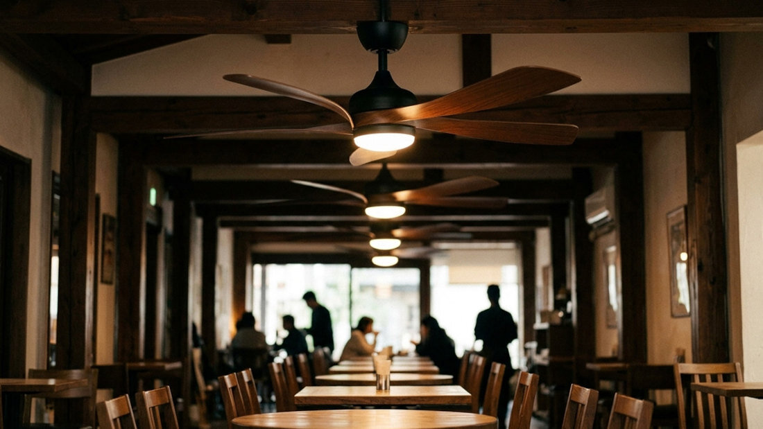 Wnętrze restauracji z drewnianymi stołami i krzesłami, na suficie zamontowane są wentylatory z drewnianymi łopatkami. W tle widać sylwetki kilku osób siedzących przy stołach.