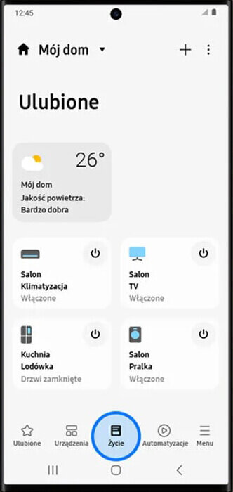 Ekran smartfona z aplikacją do zarządzania domem, pokazujący temperaturę 26°C i jakość powietrza jako \'Bardzo dobra\'. Widoczne są ikony urządzeń: klimatyzacja, TV, lodówka i pralka, z informacjami o ich statusie.