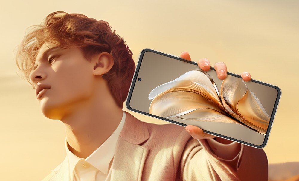 Osoba trzyma smartfon z dużym ekranem, na którym widoczna jest abstrakcyjna grafika w odcieniach złota. Tło jest jasne, a osoba ubrana jest w jasną marynarkę.