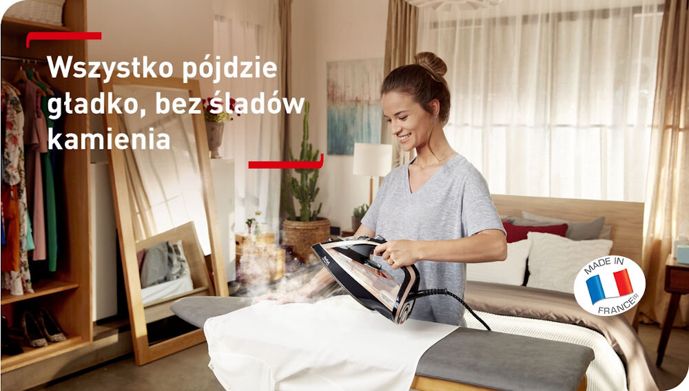 Osoba prasuje ubranie żelazkiem w jasnym pokoju. Na obrazie widoczny jest tekst: \'Wszystko pójdzie gładko, bez śladów kamienia\' oraz logo z napisem \'MADE IN FRANCE\'.