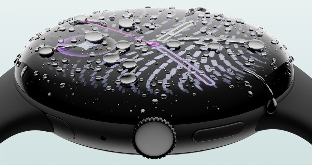 Smartwatch z okrągłym wyświetlaczem pokrytym kroplami wody, z widocznymi wskazówkami zegara w kolorze fioletowym. Obudowa jest ciemna, z widocznym przyciskiem z boku.