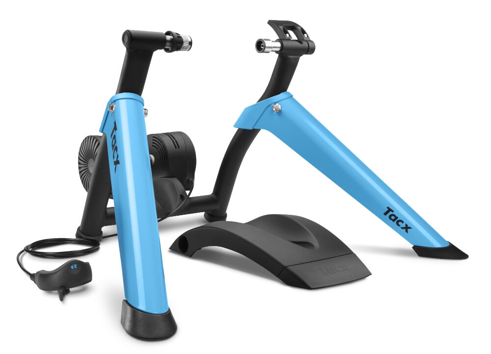 Na obrazie widoczny jest trenażer rowerowy z niebieskimi ramionami i czarną podstawą. Na ramionach znajduje się napis \'Tacx\'.