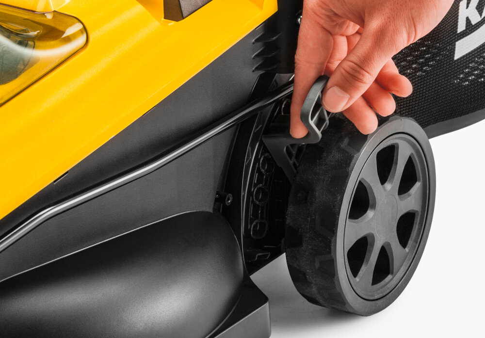 Osoba trzyma uchwyt przy kole żółtej kosiarki z widocznym logo \'KARCHER\' na czarnym tle.
