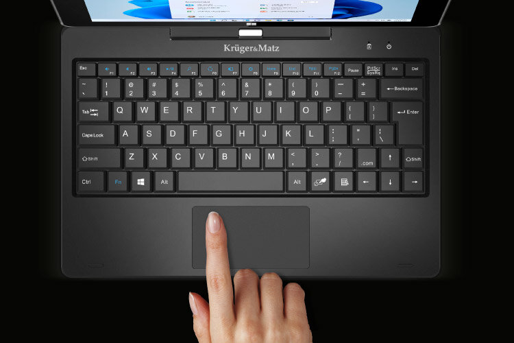 Na obrazie widoczna jest klawiatura laptopa z logo \'Krüger&Matz\' nad klawiszami. Dłoń wskazuje na touchpad poniżej klawiatury.