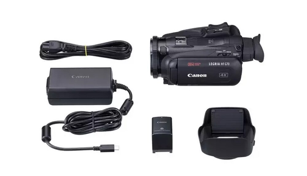 Na obrazie znajduje się czarna kamera cyfrowa z napisem \'Canon LEGRIA HF G70 4K\', obok której leżą akcesoria: ładowarka, kabel zasilający, bateria i osłona przeciwsłoneczna.