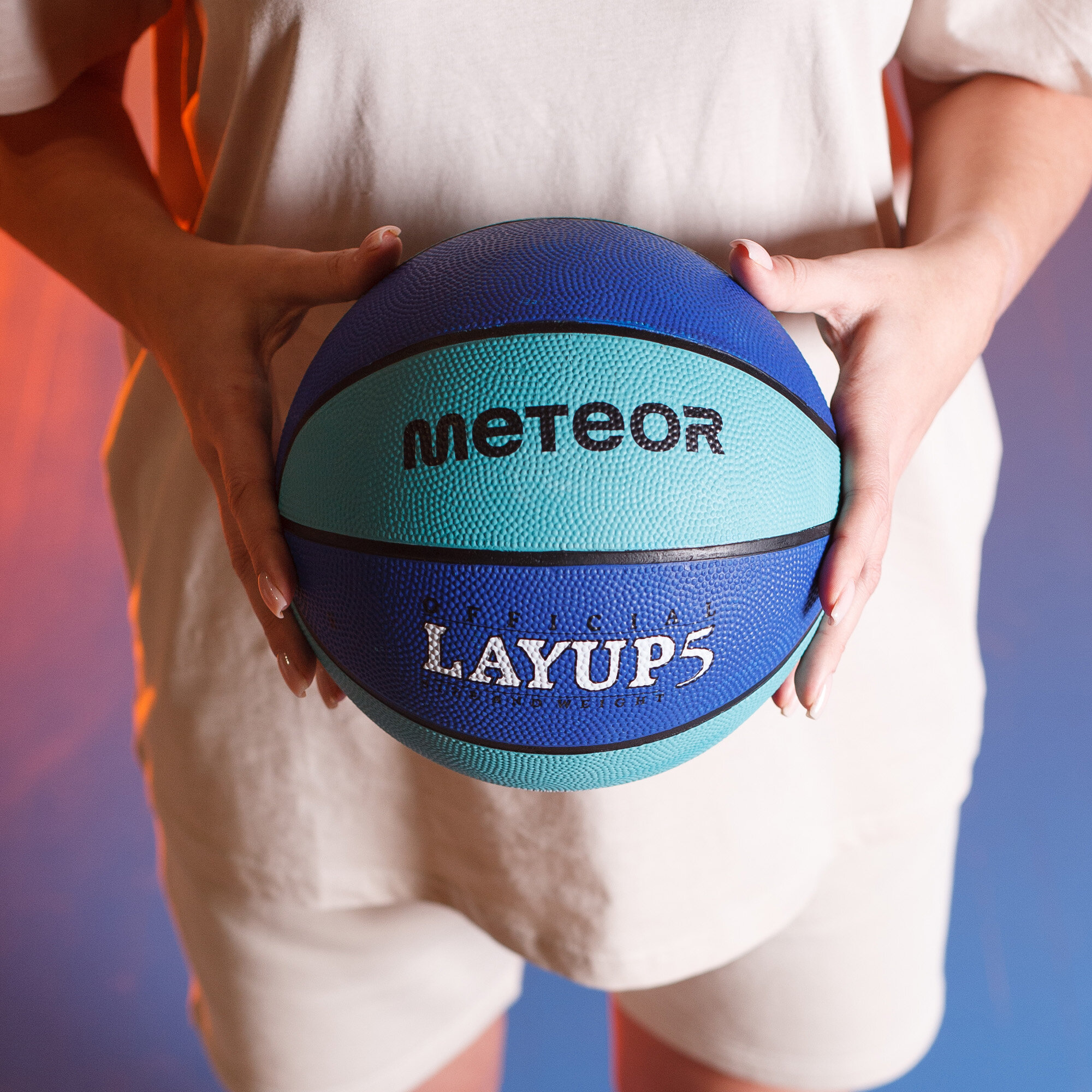 Osoba trzyma piłkę do koszykówki w kolorach niebieskim i turkusowym z napisami \'METEOR\' i \'LAYUP5\'.
