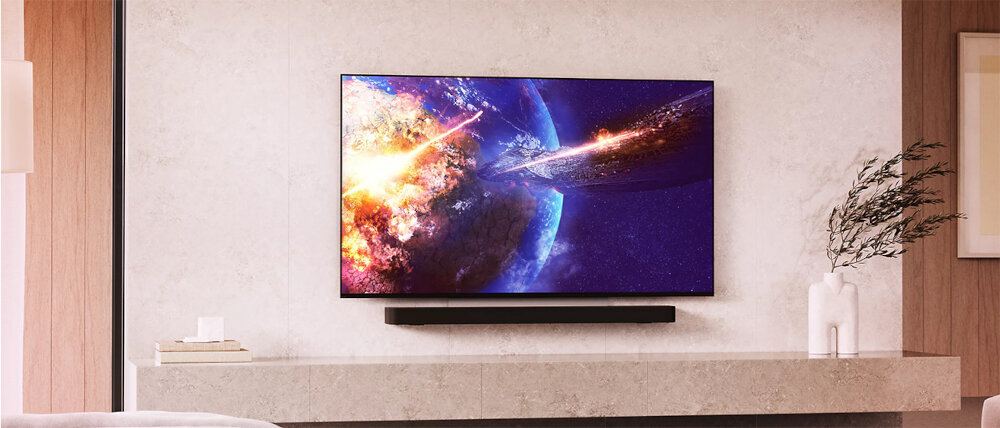 Na ścianie wisi duży telewizor wyświetlający kolorową grafikę z kosmiczną sceną. Pod telewizorem znajduje się wąska półka z dekoracyjnymi elementami.