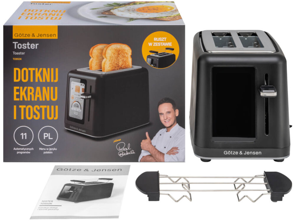 Na obrazie znajduje się czarny toster Götze & Jensen z dwoma otworami na pieczywo, obok którego leży metalowy ruszt. W tle widoczny jest karton z napisem \'DOTKNIJ EKRANU I TOSTUJ\' oraz instrukcja obsługi.