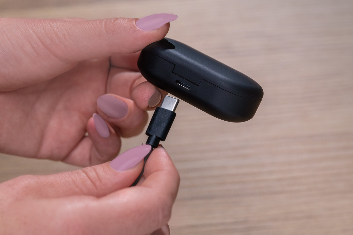 Osoba trzyma czarne etui na słuchawki douszne, do którego podłącza kabel USB-C.