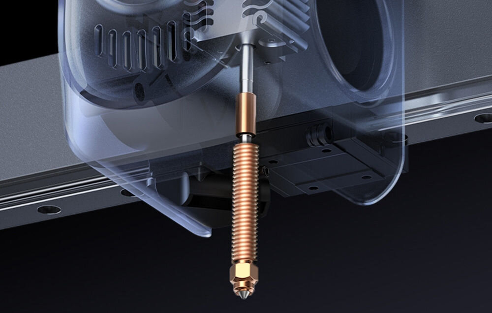 Zbliżenie na element drukarki 3D z metalowym, spiralnym komponentem w centralnej części obrazu. W tle widoczne są części mechaniczne i obudowa urządzenia.