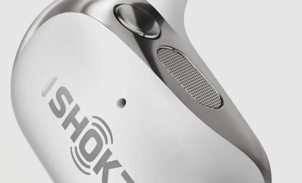 Zbliżenie na słuchawkę z widocznym logo \'SHOKZ\' oraz przyciskiem i kratką głośnika na jasnym tle.