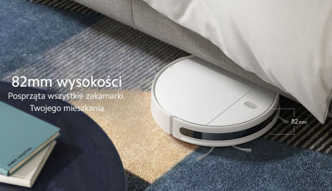 Robot sprzątający o wysokości 82 mm wjeżdża pod łóżko na dywanie. Obok widoczny jest tekst: \'82mm wysokości Posprząta wszystkie zakamarki Twojego mieszkania\'.