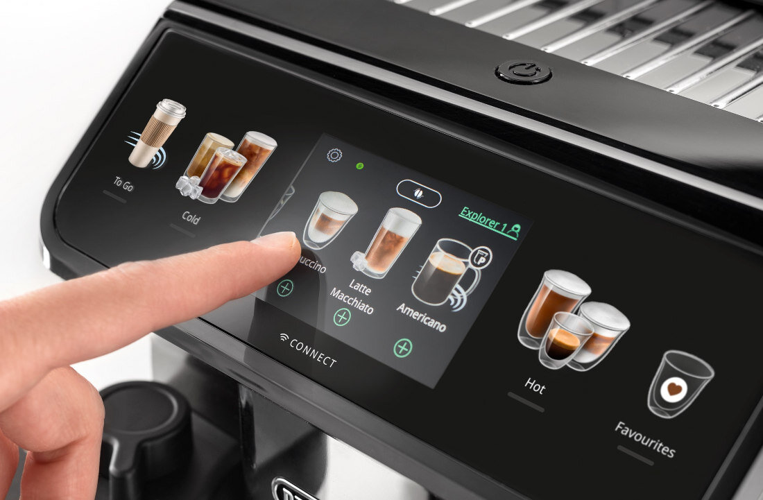 Zbliżenie na panel dotykowy ekspresu do kawy z widocznymi ikonami różnych napojów, takich jak Cappuccino, Latte Macchiato i Americano. Palec wskazuje na ikonę Cappuccino, a na ekranie widoczne są również opcje \'To Go\', \'Cold\', \'Hot\' i \'Favourites\'.