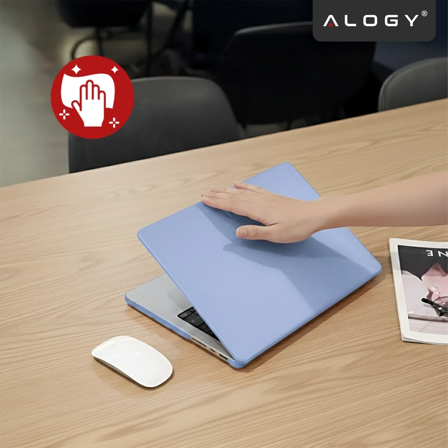 Na drewnianym stole znajduje się laptop z lawendowym etui, na którym spoczywa dłoń. Obok leży biała myszka i magazyn, a w rogu widoczne jest logo \'ALOGY\'.
