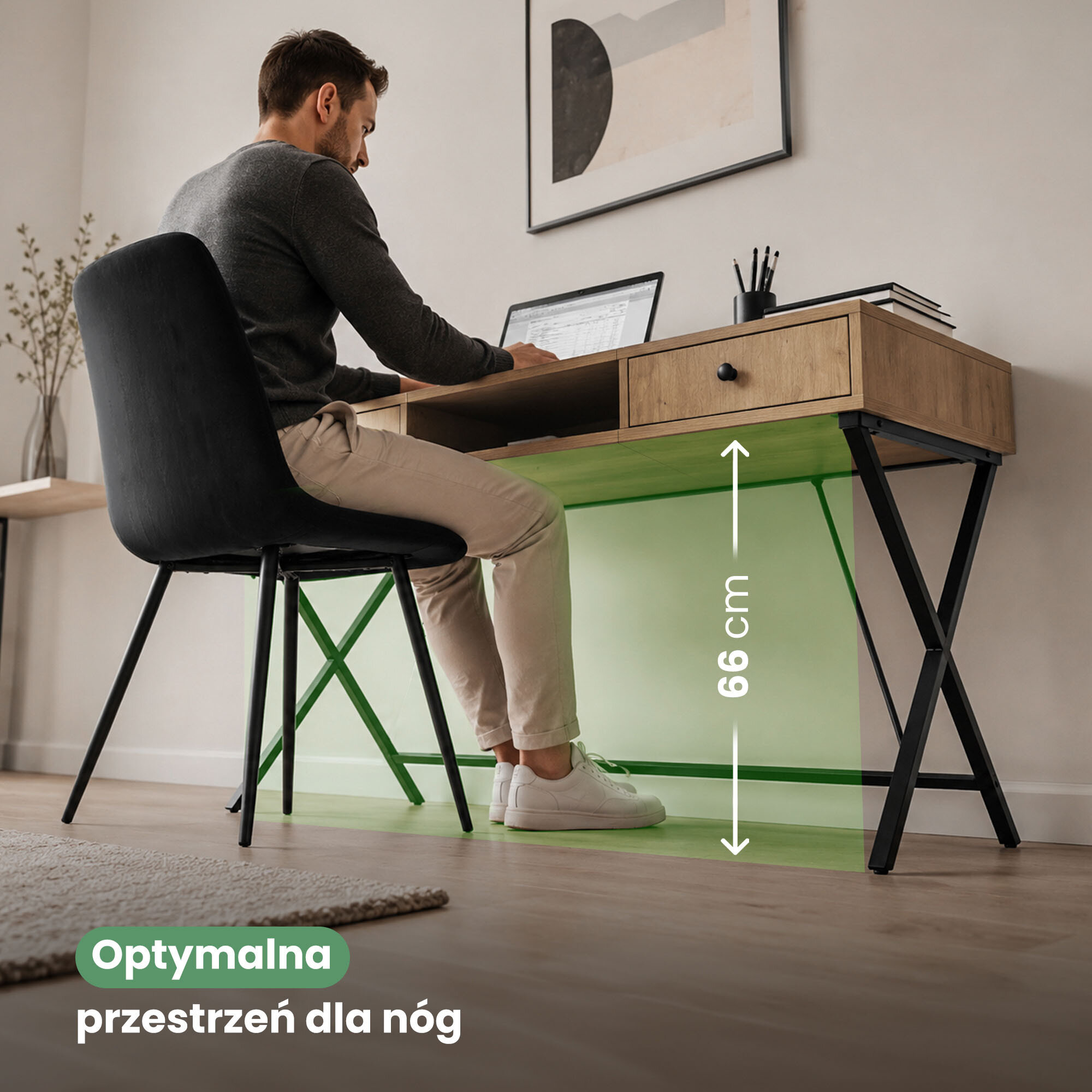 Mężczyzna siedzi przy biurku z dwiema szufladami i czarnymi nogami, na którym stoi laptop i kilka książek. Na obrazie widoczny jest tekst: \'Optymalna przestrzeń dla nóg\' oraz oznaczenie wysokości 66 cm.